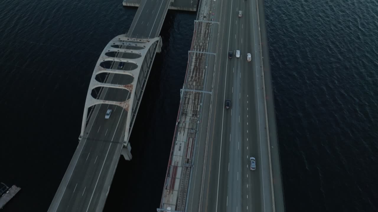 Aerial drone flight captures cars entering the floating bridge over Seattle’s tranquil blue lake. The distant sunrise casts a radiant glow