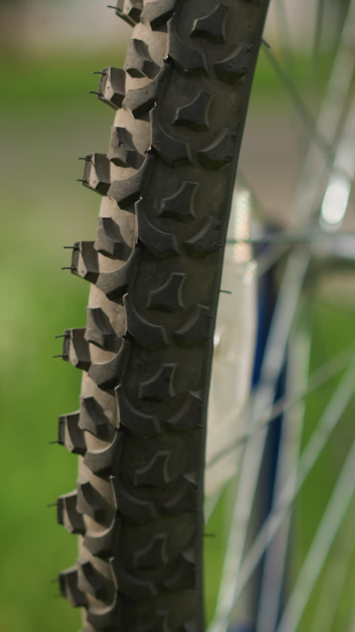 primer plano de una bicicleta colocada al revés en un campo cubierto de hierba con su neumático trasero enfocado y girando lentamente, el fondo, con vegetación y edificios, está suavemente borroso