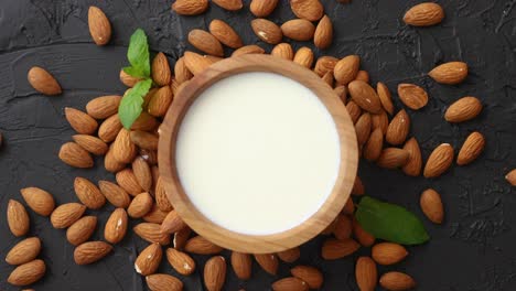 fresh almond milk in wooden bowl and almonds on black stone background
