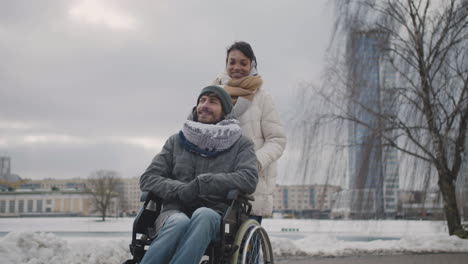 Happy-Muslim-Woman-Taking-Her-Disabled-Friend-In-Wheelchair-On-A-Walk-Around-The-City-In-Winter-1