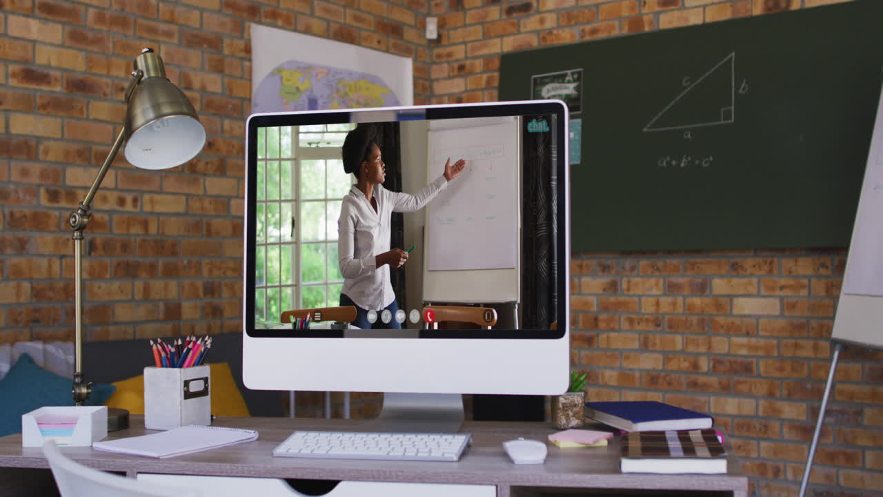 Webcam view of african american female teacher on video call on computer on table at school