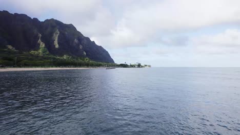 Eine-Atemberaubende-Luftaufnahme-Der-Küste-Von-Oahu-Mit-üppigen-Grünen-Bergen,-Die-Auf-Das-Ruhige-Meer-Treffen