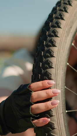 primer plano de un neumático de bicicleta trasero robusto, inspeccionado cuidadosamente para la presión del aire por una persona que lleva guantes negros, los dedos presionando firmemente, el fondo presenta un edificio suavemente borroso