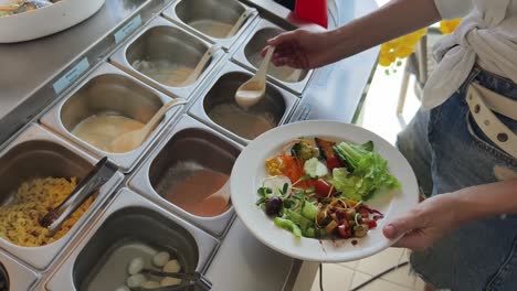 mujer que se sirve ensalada en un buffet de autoservicio