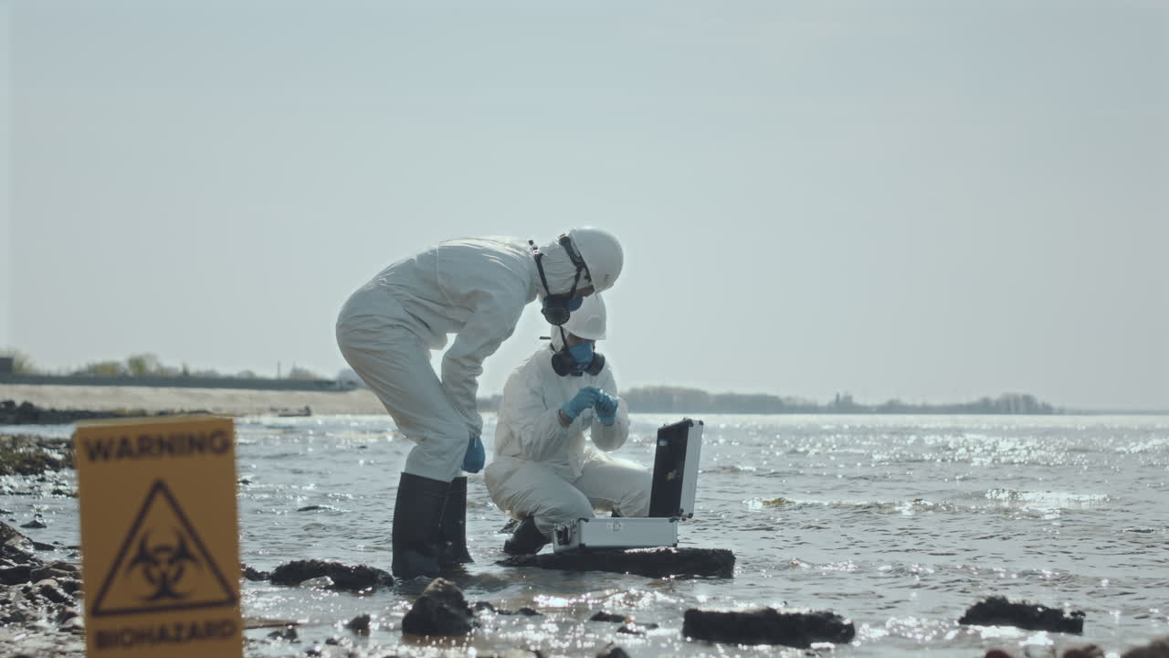 Two Ecologists in Coveralls Working in Polluted Area