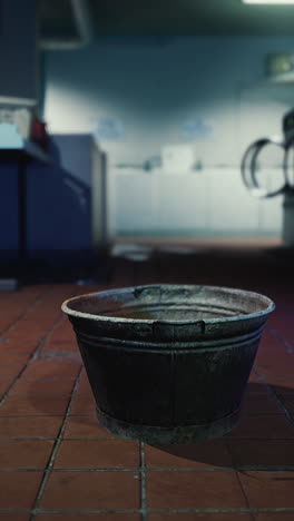 a rusty metal bucket on a dirty tile floor