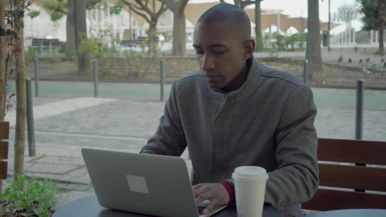 Uncertain young man using laptop outdoor