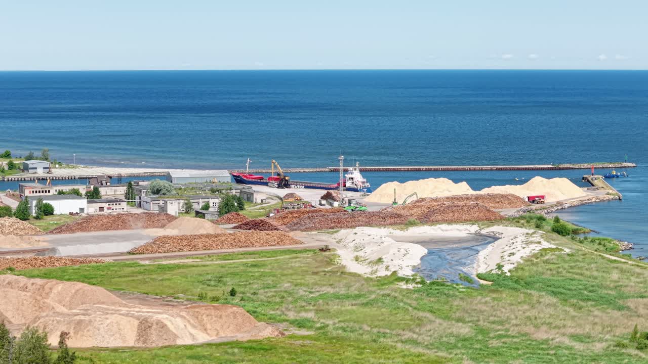 Drone of cargo ship docked at port surrounded by warehouses, roadways, and calm sea