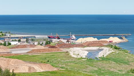 drone of cargo ship docked at port surrounded by warehouses, roadways, and calm sea