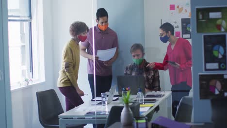 diversos colegas con máscaras faciales trabajando juntos en la sala de reuniones de una oficina moderna