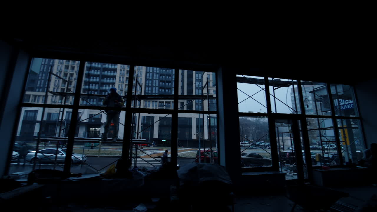 Footage from inside the dark interior of the unfinished building. Builders work inside and outside the room.