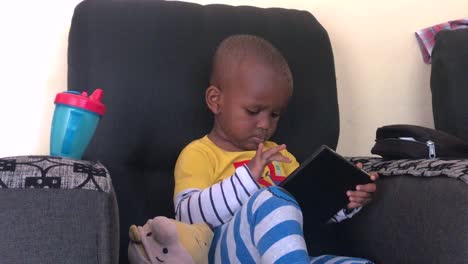 Close-up-of-a-young-African-boy-playing-on-a-tablet-computer,-while-sitting-in-a-chair-in-his-home