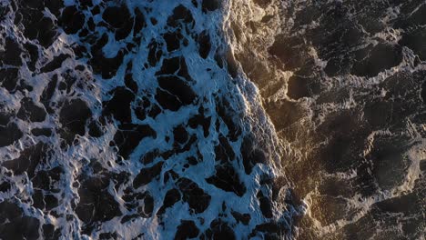 aerial top down flying slowly forward as a couple of wind whipped waves pass over a dark ocean with cool patterns in the surf in york beach maine