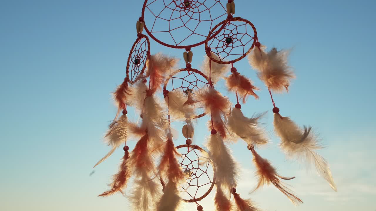 el cazador de sueños con plumas naranjas gira, balanceándose con el viento ligero en cámara lenta contra el fondo del cielo azul a la luz del atardecer en verano. estilo boho en un día soleado. amuleto de estilo indio. vintage. macro