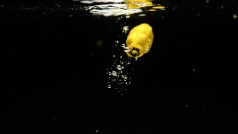 super slow motion of fresh madame jeanette peppers falling into water on black background