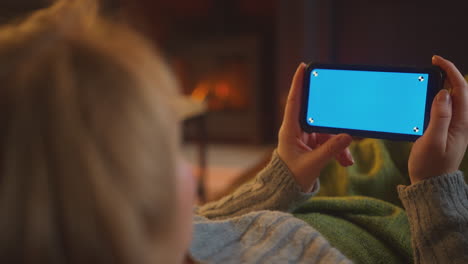 close up de la mujer en casa acostado en la sala de estar con el fuego de transmisión en la pantalla azul del teléfono móvil