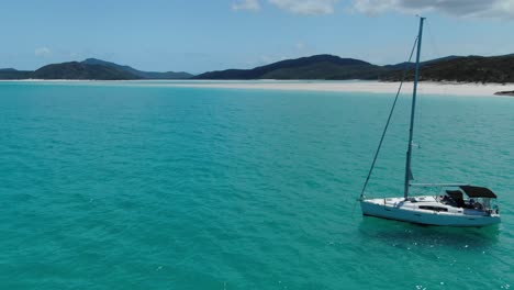 Un-Yate-De-Vela-Blanco-Está-Anclado-Frente-A-La-Costa-De-La-Increíble-Playa-White-Haven,-Australia,-órbita-De-Drones-Y-Sobrevuelo