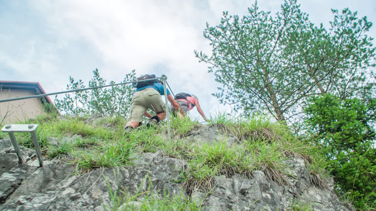 Pareja de excursionistas llegando a la cima de la escarpada pared de roca, señal de victoria