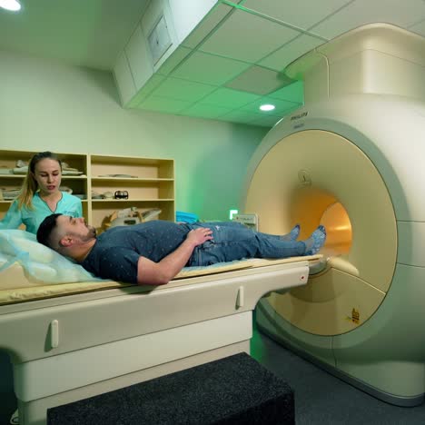 advanced medical technologies in hospital. man patient lying in magnetic resonance image device. female technician helps the patient near mri device.