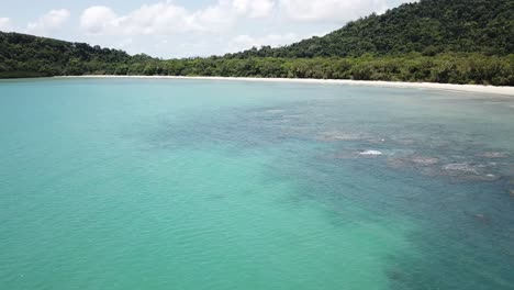 Drone-aerial-over-tropical-blue-water-and-coral-reefs-next-to-beach-and-rainforest