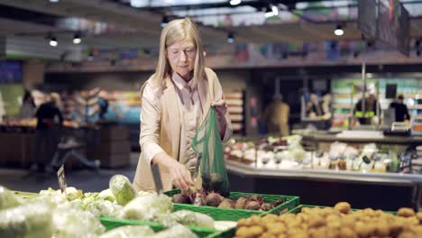 senior woman chooses and picks vegetables and puts them in an eco bag or fruits in supermarket. mature female customer standing a grocery store near the counter throws