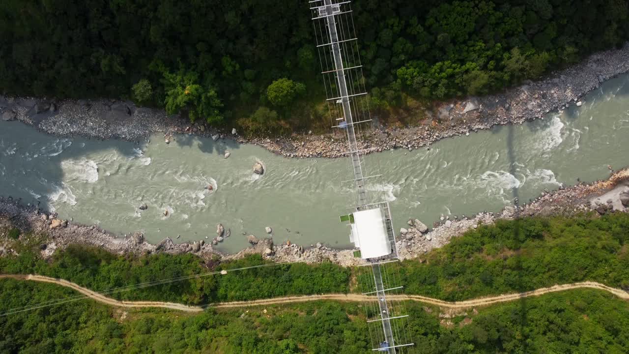 fotografía aérea de arriba hacia abajo de un río y un puente colgante en nepal durante un día soleado