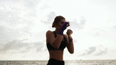 Mujer-Joven-Atlética-Haciendo-Boxeo-De-Sombra-Junto-Al-Mar-Contra-El-Hijo.-Hermosa-Boxeadora-Entrenando-En-La-Playa-Por-La-Mañana