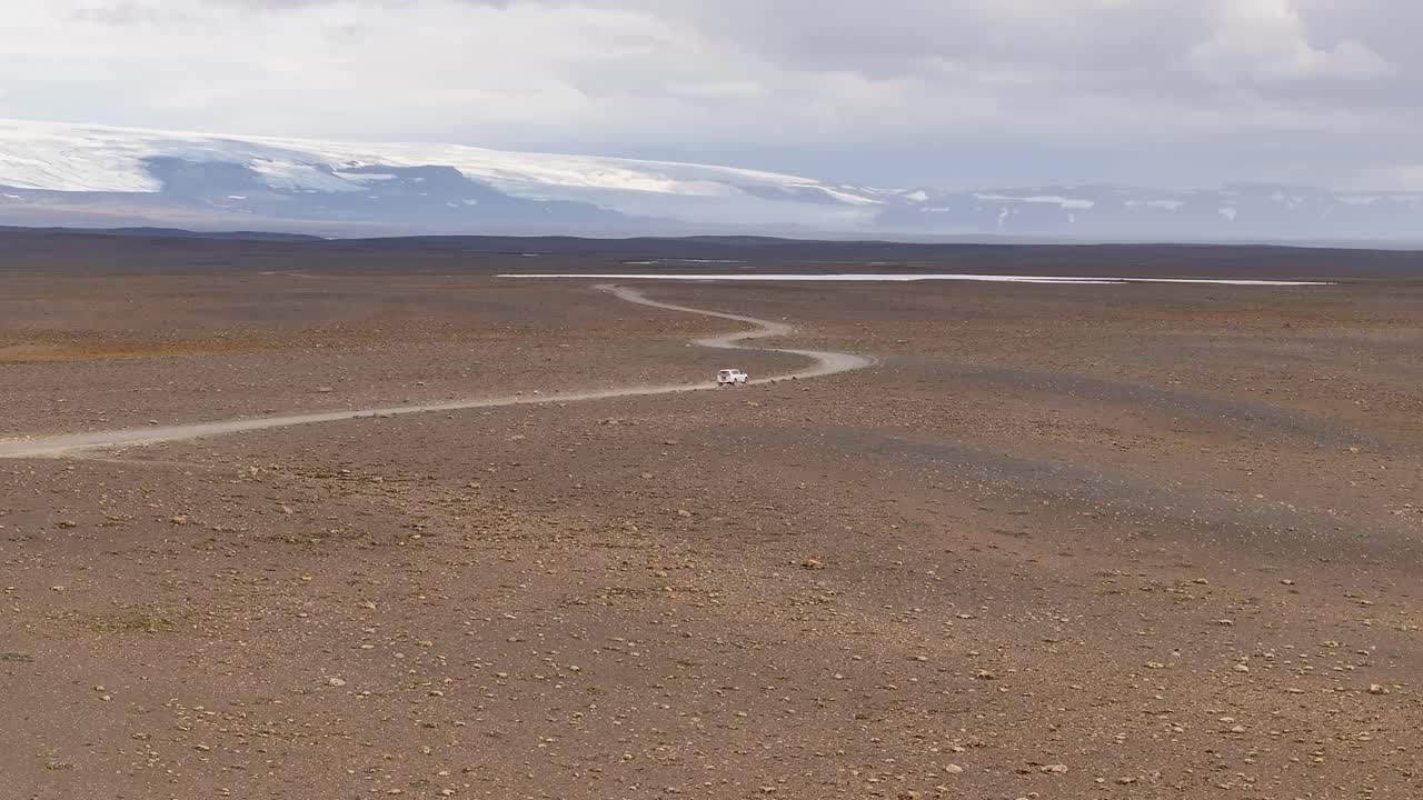 White 4x4 vehicle driving on Kjalvegur road in Iceland. Glacier and snowy peaks in background. Aerial tracking shot. Zoom