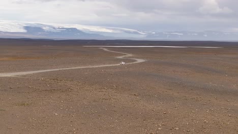 White 4x4 vehicle driving on Kjalvegur road in Iceland. Glacier and snowy peaks in background. Aerial tracking shot. Zoom