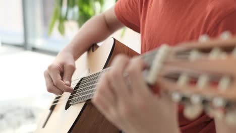 Teenage boy playing guitar while sitting on sofa at home, play the musical instrument. The concept of learning to play a musical instrument. High quality FullHD footage