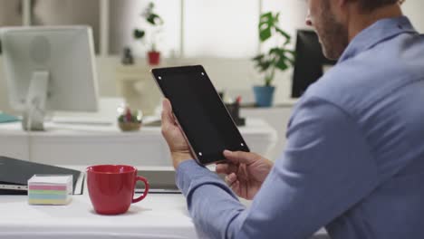 hombre de negocios caucásico teniendo una reunión de videollamadas usando una tableta en una oficina vacía