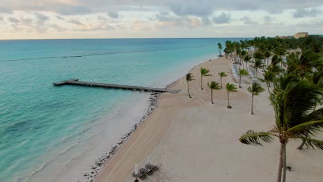 playa tropical aérea con palmeras, embarcadero de madera y horizonte marino