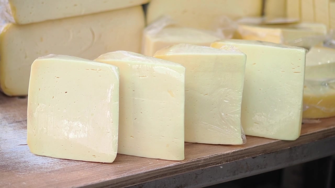 Blocks of Fresh Cheese Wrapped in Plastic on a Wooden Market Stall