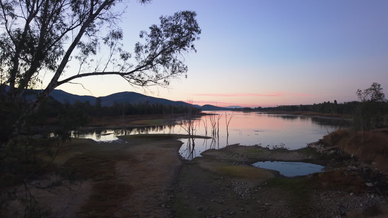 Silhouet af træer ved en sø i Californien. Otay Lakes i Chula Vista, Californien, droneflyvning fremad ved solopgang med smukke morgenfarver
