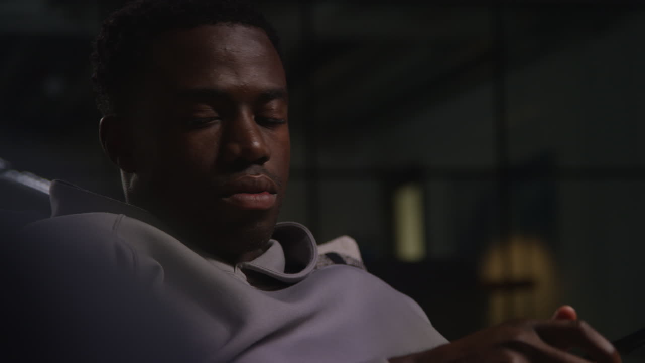 Close Up Of Unhappy And Depressed Young Man Sitting On Sofa At Home Checking Messages Or Online On Mobile Phone At Night