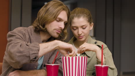 glückliches paar, das popcorn isst, während es an der kino-snackbar redet und lacht