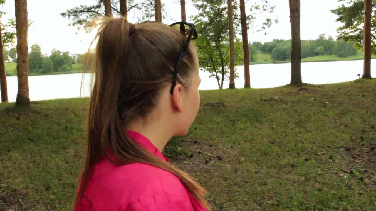 Menina caminhando no parque ao lado de um lago.