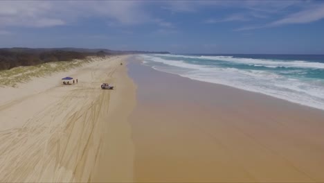 low aerial drone shot travelling north up main beach on queensland's north stradbroke island towards a camp site, with 4x4 four wheel drive vehicles driving on the beach