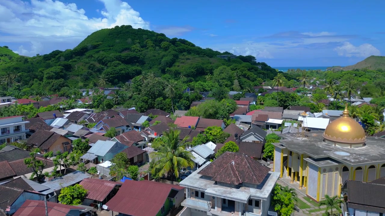 Endonezya'nın Lombok adasındaki Gerupuk köyü, yerel evleri, bir camisi ve koyu çevreleyen çok sayıda balıkçı teknesiyle. Büyüleyici havadan görünüm, sağa dönen drone panoraması.