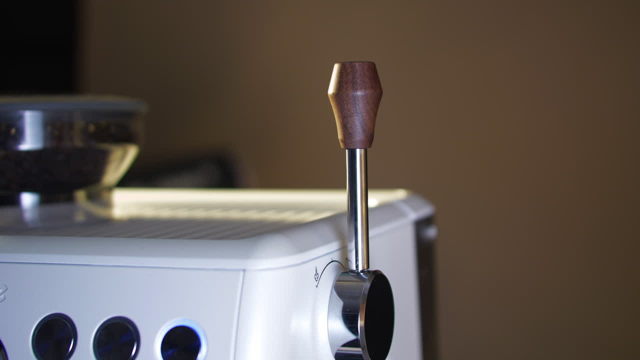 Close up of a female hand pulling the steam lever forward on a portafilter espresso machine to activate the milk steamer. Warm café lighting highlights control, pressure, and professional coffee prepa