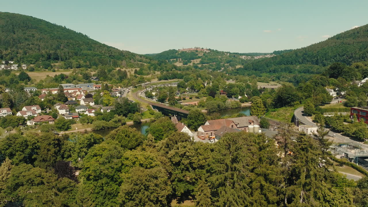 Primo piano aereo che rivela da dietro gli alberi una città rurale tedesca, mostrando le case, il canale e il paesaggio dell'Odenwald