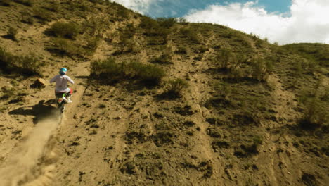 person in helmet rides motorcycle along bushy hill fpv drone. sportsman on motorcycle enjoys offroad racing at desert highland. moto sport contest