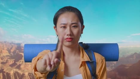 close up of asian female hiker with mountaineering backpack showing no gesture with index finger while traveling at the top of mountain