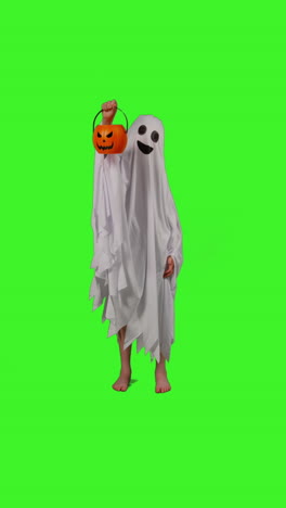 Vertical-Video-Full-Length-Shot-Of-Child-Dressed-Up-In-Ghost-Costume-Trick-Or-Treating-At-Halloween-Holding-Pumpkin-Shaped-Jack-O'Lantern-Bucket-Against-Studio-Green-Screen