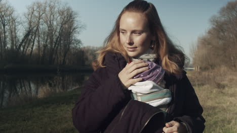 Young-mother-walks-outside-with-baby-on-cool-day,-tracking