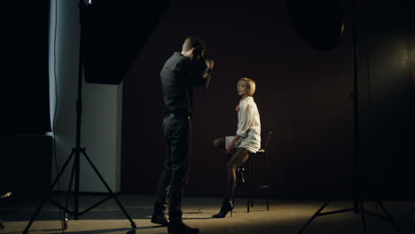 distant view of caucasian young female model posing in the dark studio while the photographer taking shots of her