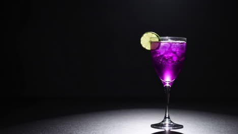 vibrant purple cocktail with lime garnish in spotlight