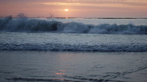 sunrise reflecting on the water as a wave comes crashing down in slow-motion