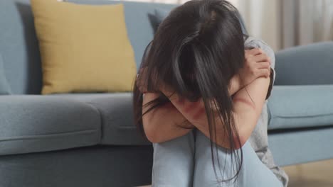 close up of young asian woman victim of violence with bruise on body sitting hugging her knees and crying on the floor at home