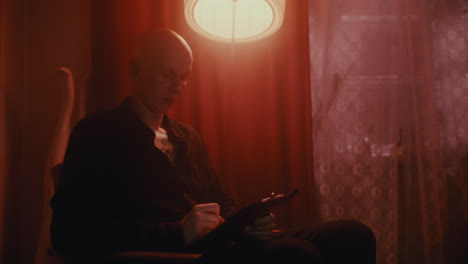 bald man writing in a dimly lit room